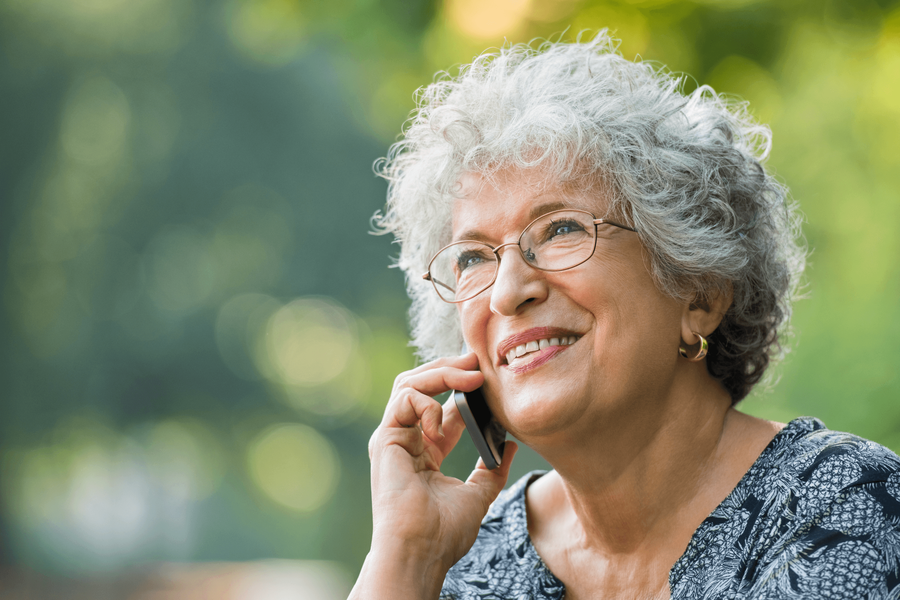 A smiling older woman talking on the phone outdoors
